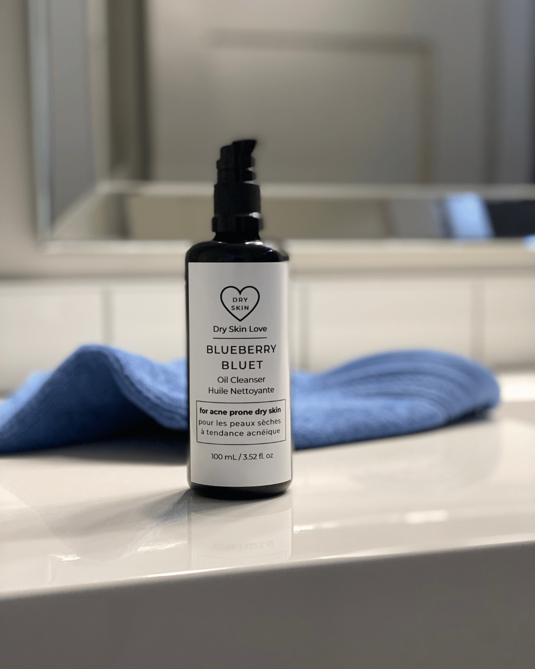 Bottle of Blueberry Oil Cleanser on a bathroom counter with a blue towel, luxury face cleanser