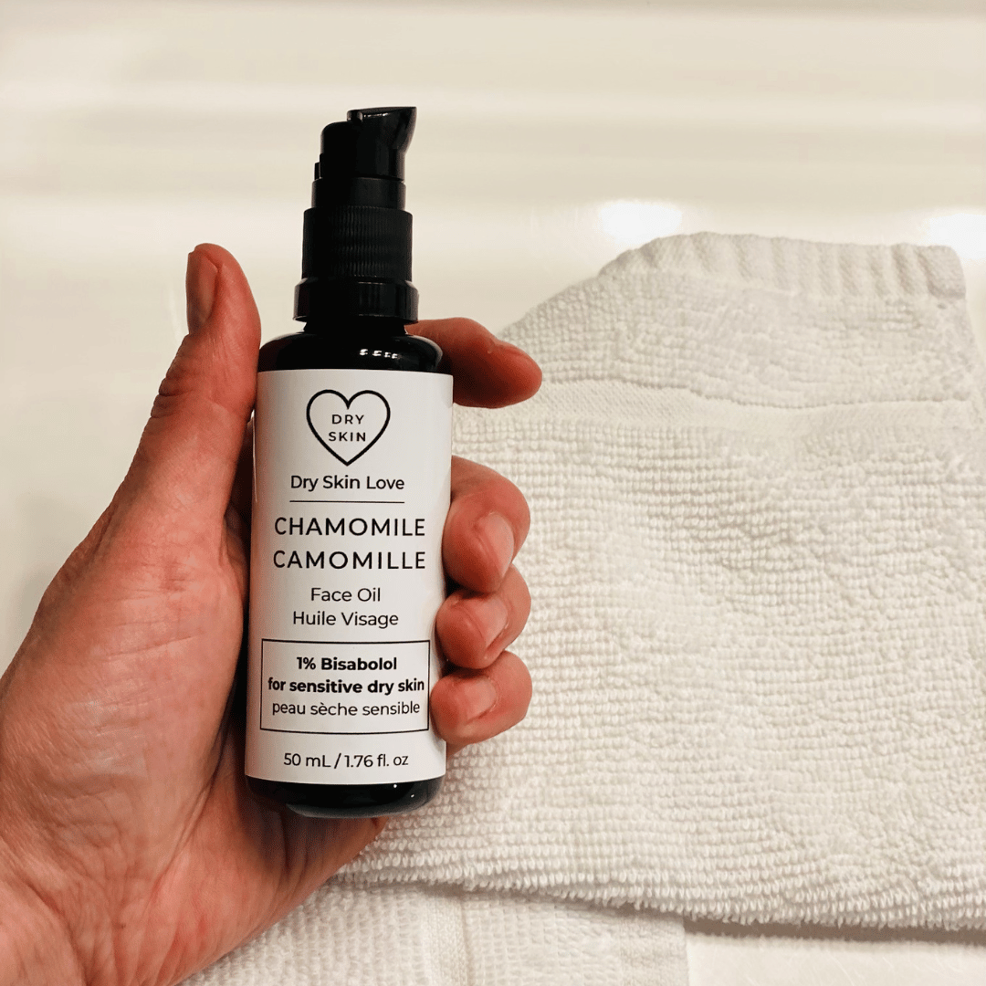 Hand holding a bottle of 'Dry Skin Love Chamomile 1% Bisabolol Face Oil' for Sensitive Skin on a white cloth on a white counter, luxury face oil
