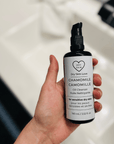 Hand holding a bottle of 'Dry Skin Love Chamomile Oil Cleanser for Sensitive Skin' over a white sink, Luxury Face Cleanser 