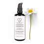Miron violet glass bottle of chamomile face cleanser displayed with a fresh chamomile flower on a white background, Dry Skin Love Chamomile Oil Cleanser for Sensitive Skin.