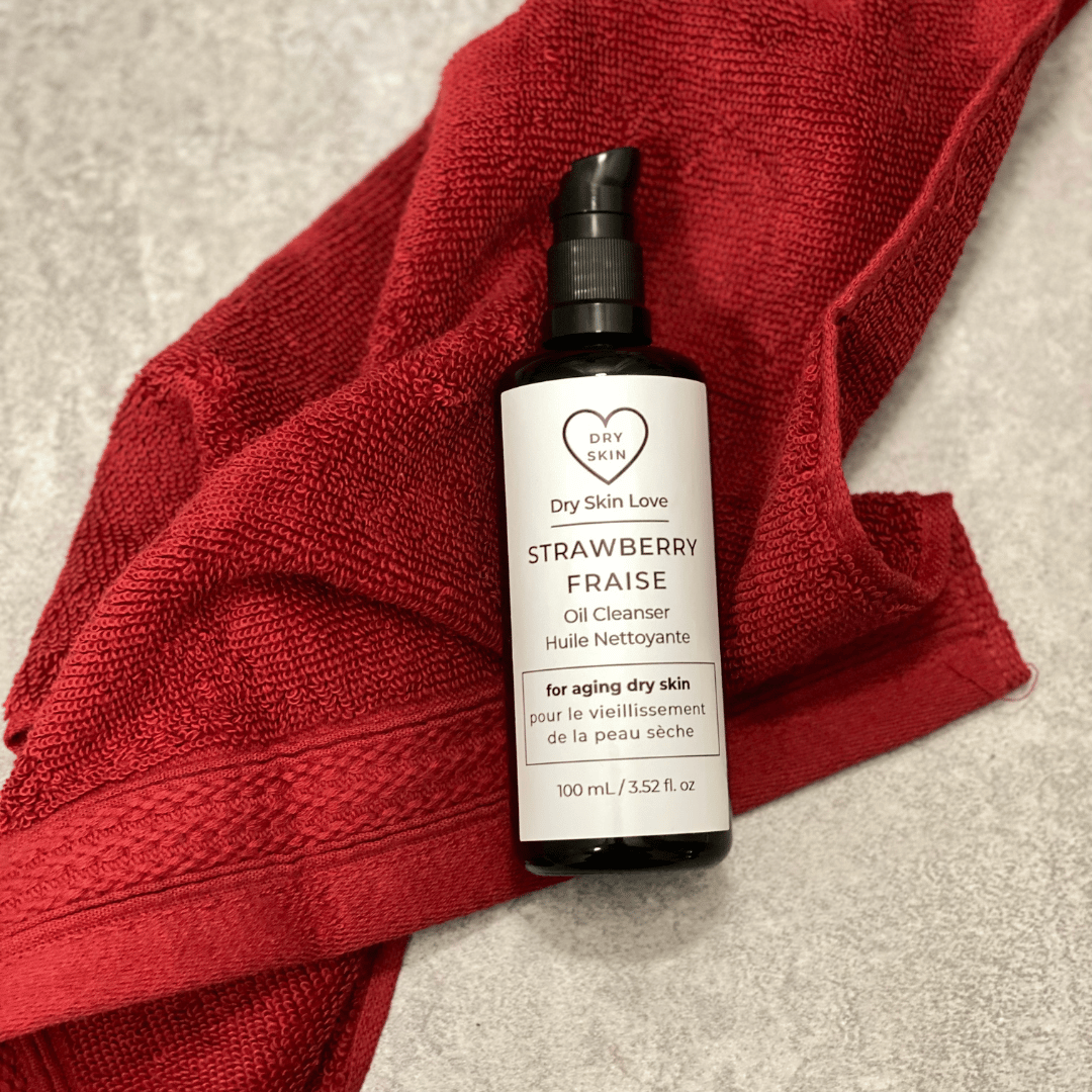 Bottle of 'Dry Skin Love Strawberry Oil Cleanser' with a red towel in the background, Luxury Face Cleanser for Dry Aging Skin